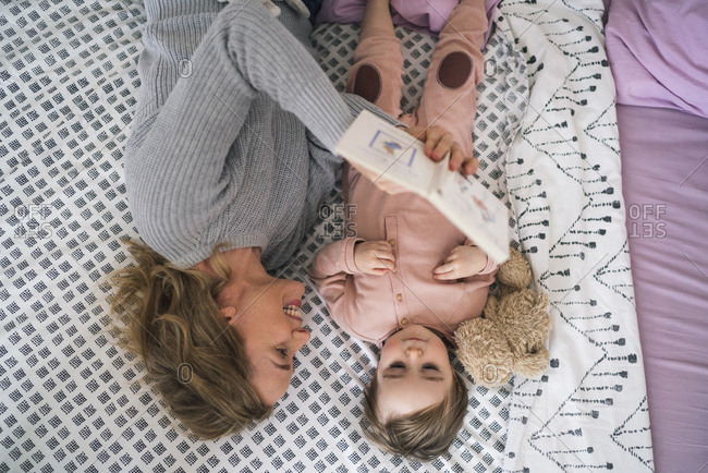 Top view of mother and daughter lying on a bed and reading an illustrated book