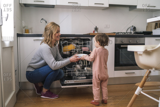 Daughter helps her mom to put dishes away from a dishwasher
