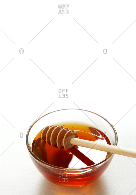 Clear bowl of amber honey with a honey dipper on a white seamless background