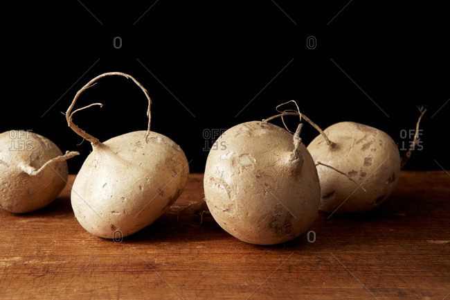 Detailed view of four jicama roots on a dark wood cutting board
