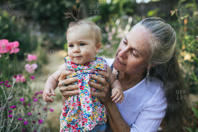 A grandmother holds her baby granddaughter in a garden