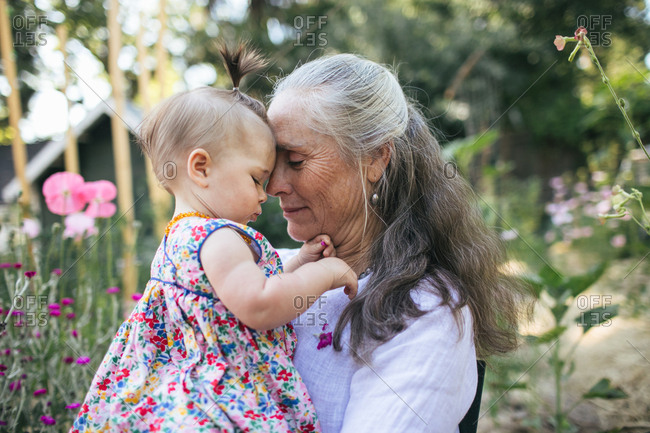 A grandmother and her granddaughter sit in a garden, foreheads together