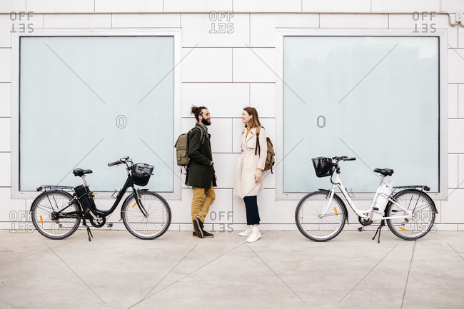 Man and woman with e-bikes standing at a building talking