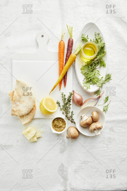 Cutting board with an assortment of vegetables, cheese and pita bread. Also a cut lemon.