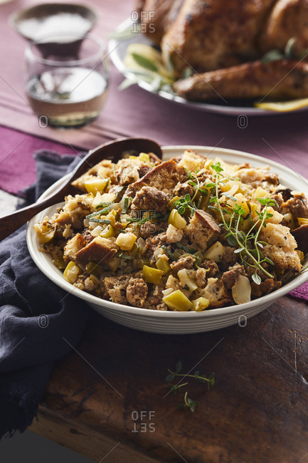 Bowl of homemade stuffing with a wooden spoon on a wooden table set next to a blue napkin.