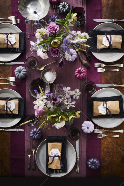 Table set with plates and name tags and purple runner and flowers.
