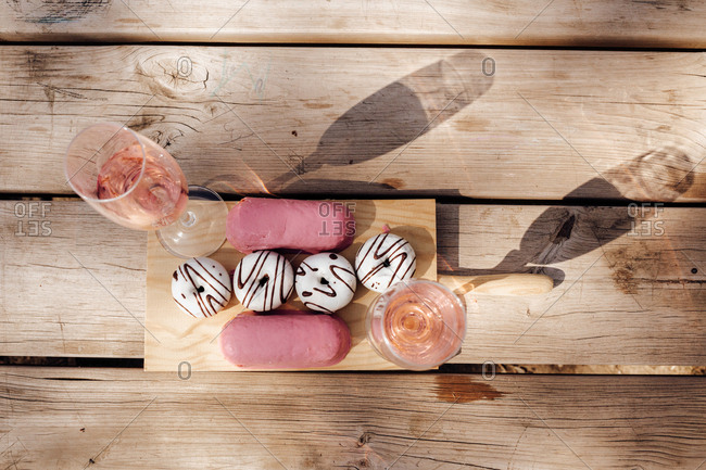Glasses with fine pink wine placed on wooden surface near set of fresh delicious doughnuts