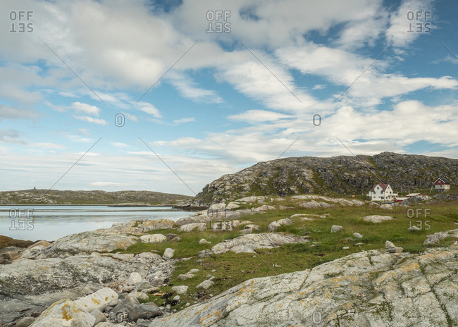 Laconic northern summer countryside with rocky hills, lake and rural houses in shiny day