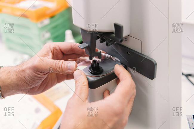 Hands of anonymous optometrist using professional tool to make lens for spectacles in laboratory