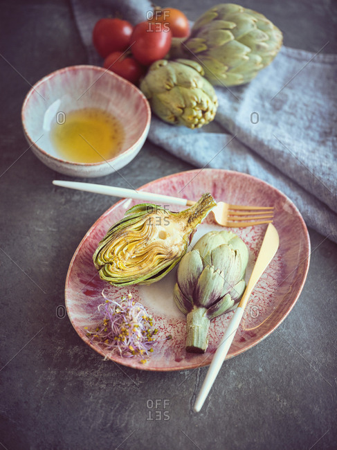 Small knife and fork and cut and whole fresh artichokes placed on pink ceramic plate on table