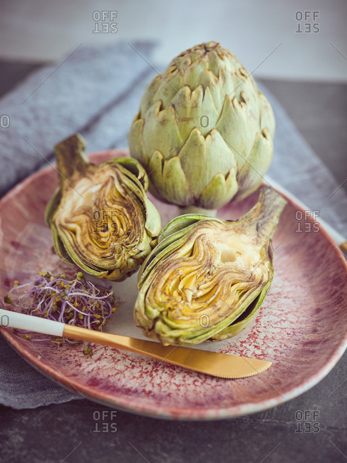 Small knife and cut and whole fresh artichokes placed on pink ceramic plate on table