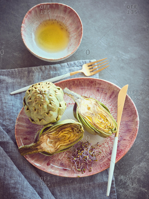 Small knife and fork and cut and whole fresh artichokes placed on pink ceramic plate on table