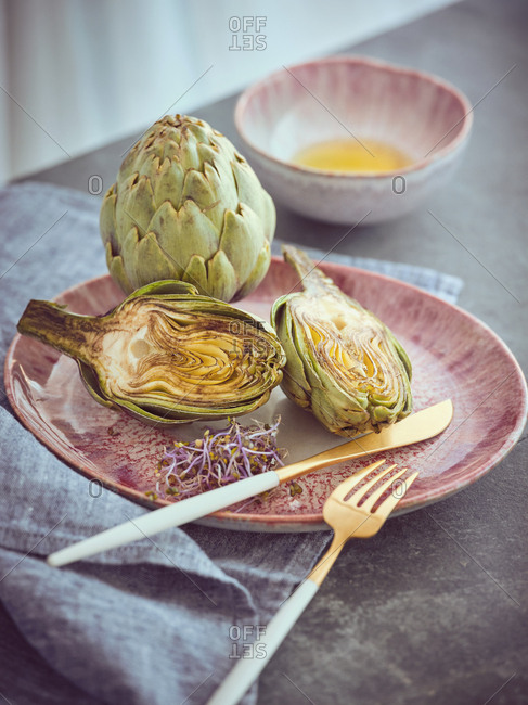 Small knife and fork and cut and whole fresh artichokes placed on pink ceramic plate on table