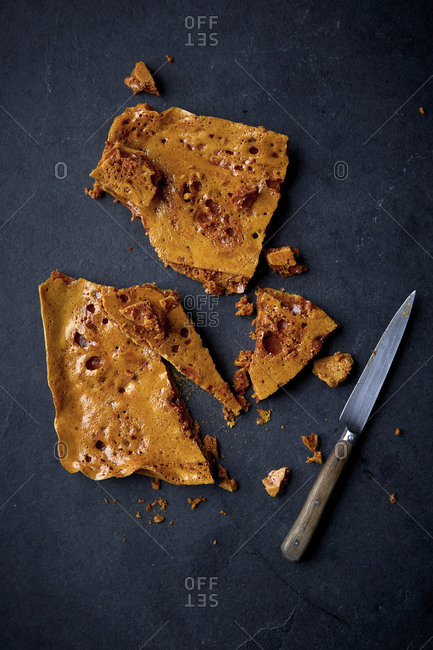 Shards of honeycomb candy with a knife on a black counter top.