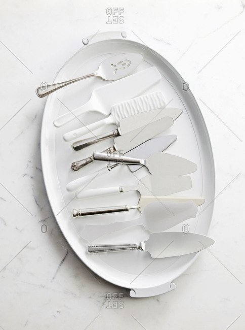 A tray filled with several different cake and pie lifters slicers and spatulas, sitting on a marble counter top.