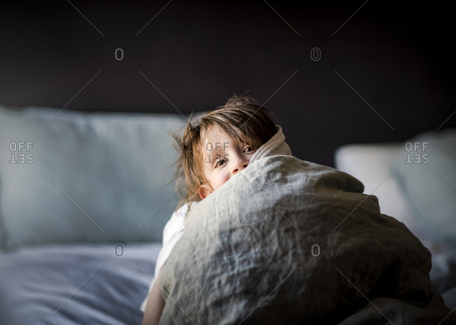 A Small Young Boy Playing Peek-A-Boo In A Bed With Blankets