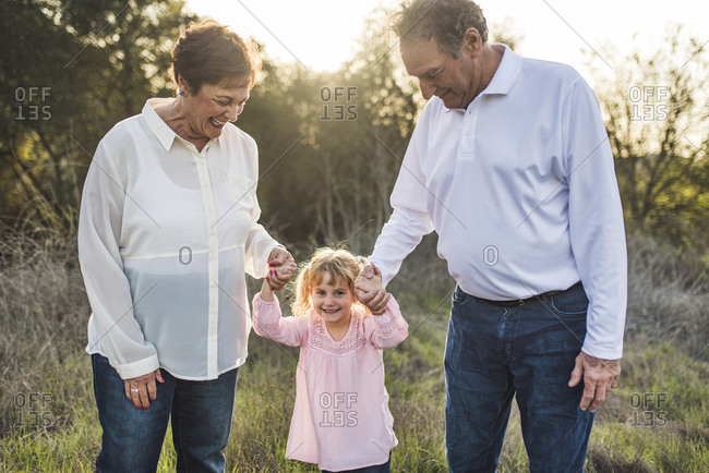 Portrait of grandparents holding little girls hand in field
