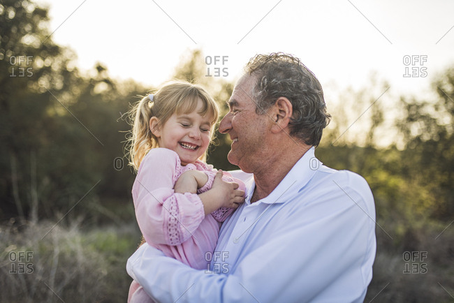 Grandpa holding granddaughter in field and laughing