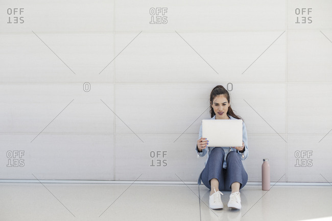 Woman sitting on floor with laptop by white wall