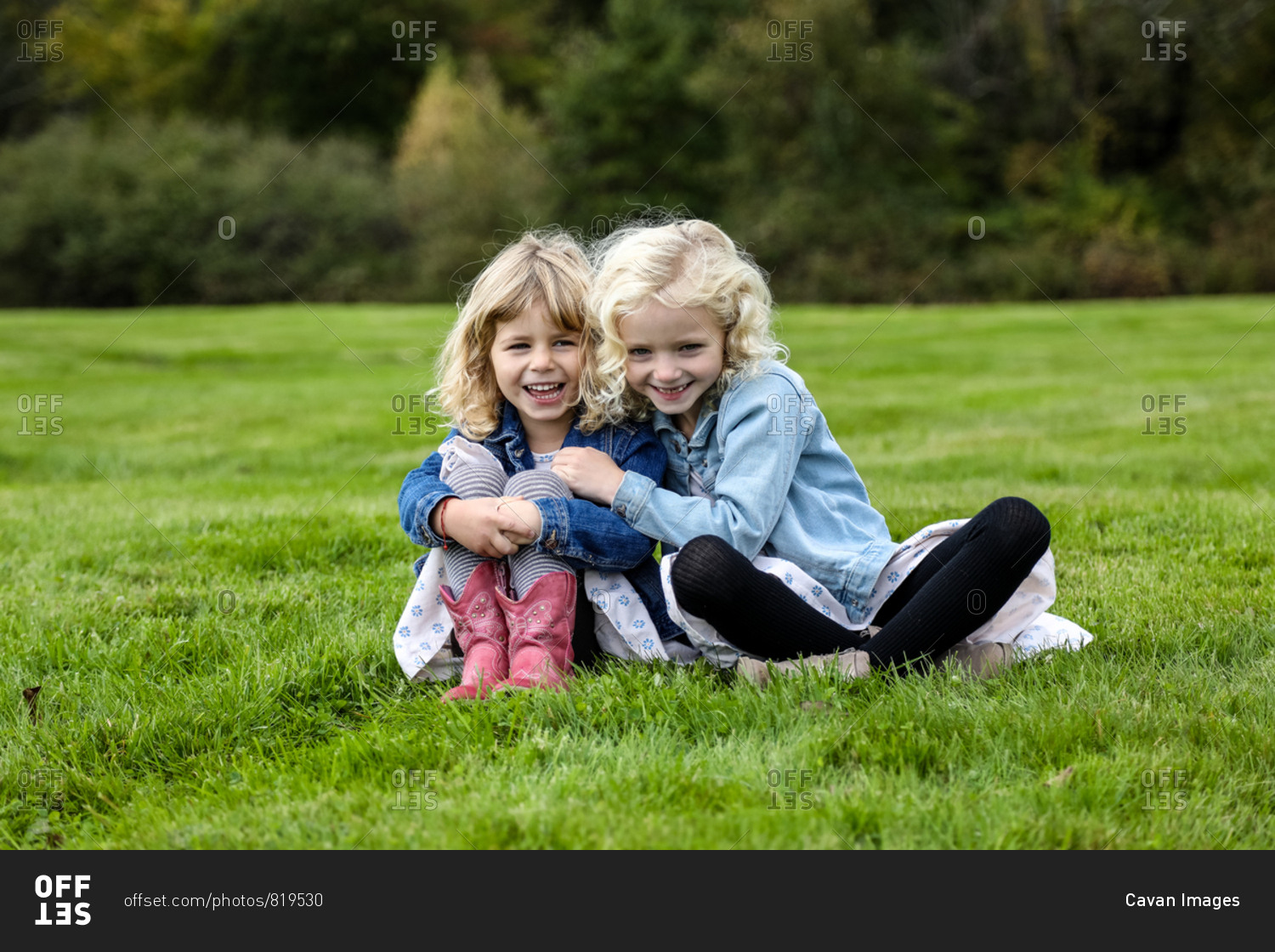 two sisters sitting on grass smiling towards camera linked arms
