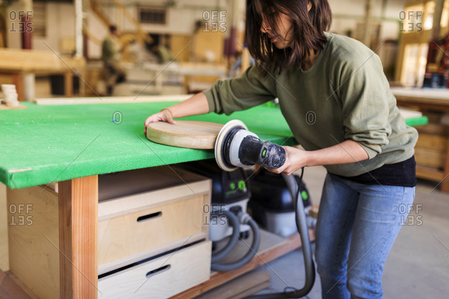 Female carpenter sanding down a wooden piece in woodshop