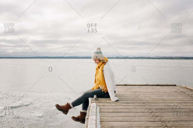 blonde woman sitting on the edge of a pier jetty smiling kicking feet