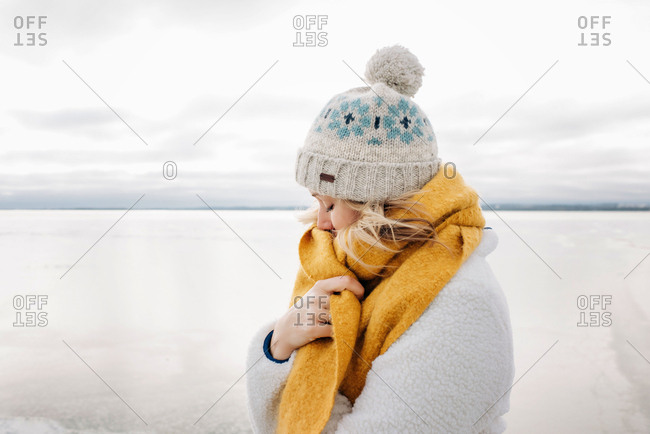 portrait of blonde woman keeping warm at the beach in winter thinking