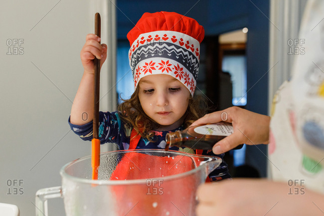 A young girl bakes with her mom wearing a chef's hat