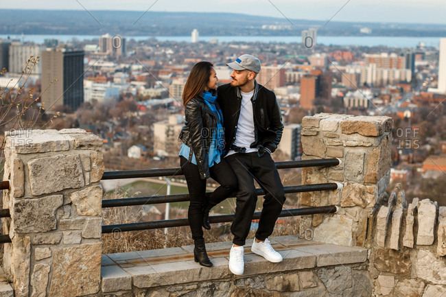 Young couple sitting on a fence overlooking the city