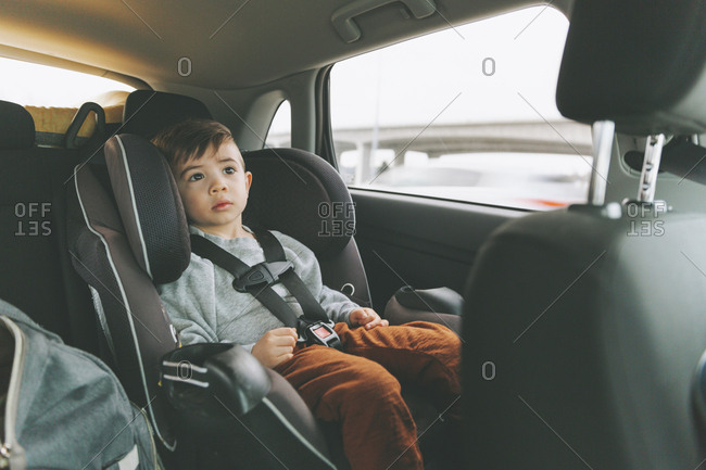Little boy sitting in car on child's seat with fastened seat belt