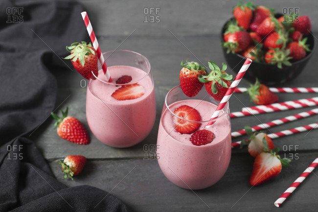 Glasses of strawberry smoothie and strawberries on dark wood