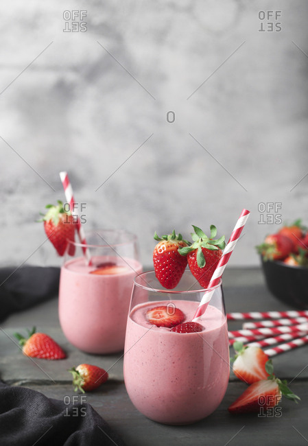 Glasses of strawberry smoothie and strawberries on dark wood