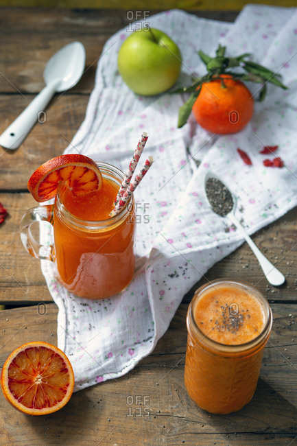 Jar of yummy fresh citrus juice with slice of ripe blood orange and straws placed on timber tabletop near napkin