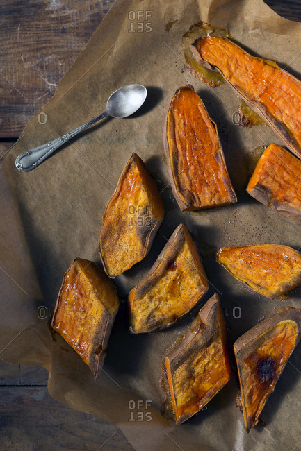 Piece of parchment paper with spoon and pieces of tasty baked Sweet potato placed on wooden table