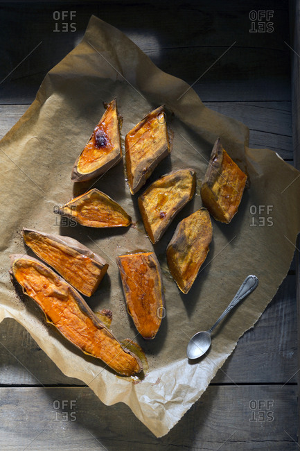 Piece of parchment paper with spoon and pieces of tasty baked Sweet potato placed on wooden table