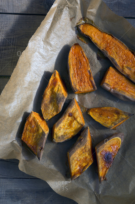 Piece of parchment paper with spoon and pieces of tasty baked Sweet potato placed on wooden table