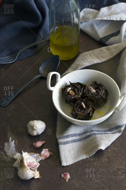 Delicious fried artichokes with aromatic garlic and oil placed in ceramic bowl near napkin and utensils