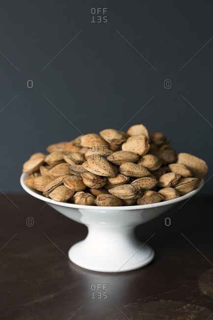 Ceramic bowl full of fresh almonds with shell placed on brown table against brown background