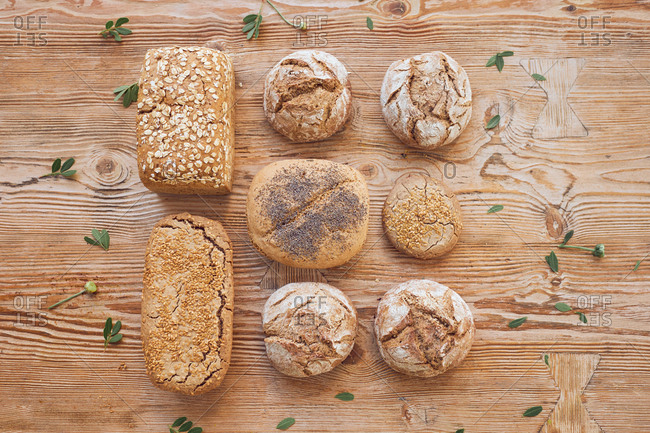 From above composition of fresh hot tasty bread loaves, buns and baguettes on wooden table in bakery