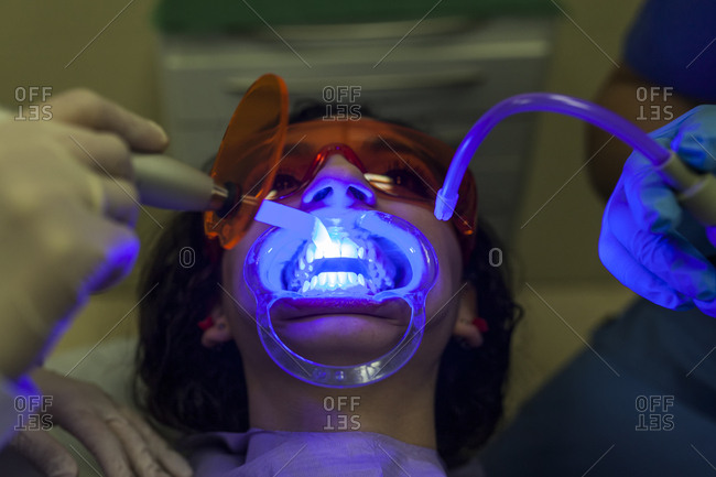 Dentist and assistant hands examining and doing ultrasonic clear young female patient teeth with special equipment with blue light in dentistry