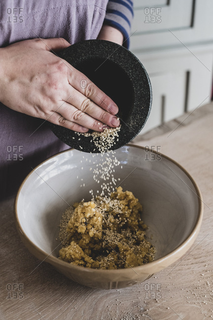 High angle close up of person adding sesame seeds to dough in a mixing bowl.