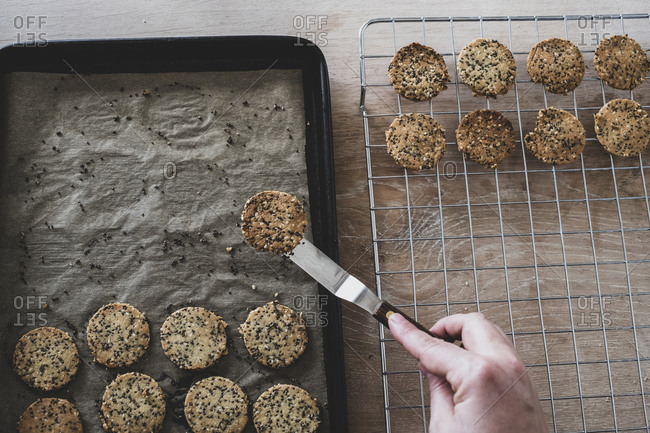 High angle close up of person removing freshly baked seeded crackers from a baking tray.
