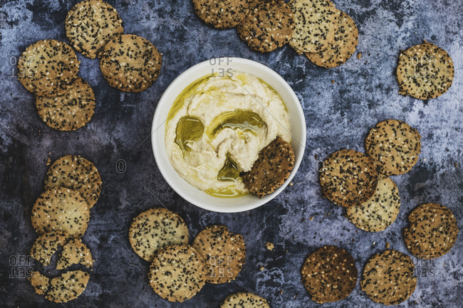 High angle close up of a bowl of hummus and freshly baked seeded crackers.