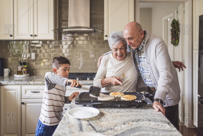 Adult son hugging mother while cooking pancakes with young grandson