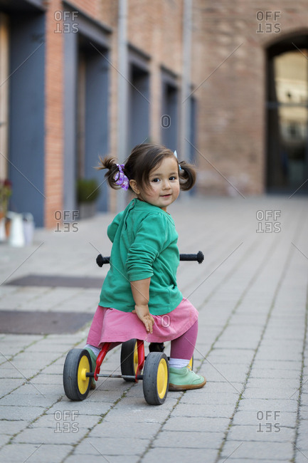 Little girl riding tricycle on patio
