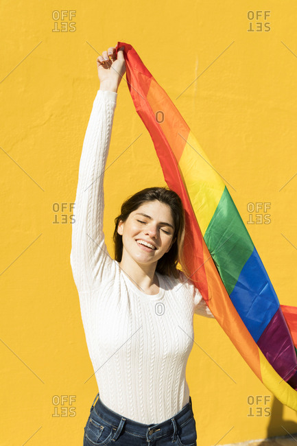 Portrait of a young woman with rainbow flag in front of yellow wall