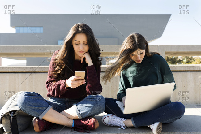 Two friends using electronic devices on outdoor steps in Barcelo