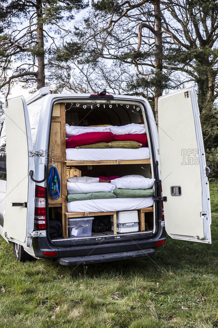 Rear view of camper van parked on a meadow, stacks of mattresses and bedding in back of vehicle.