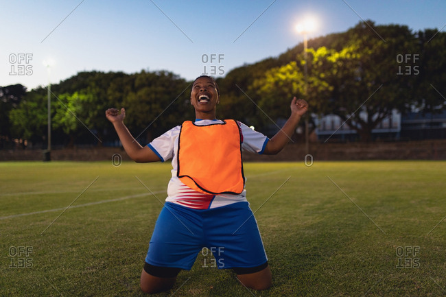 Front view of carefree African-American female soccer player cheering after victory at sports field