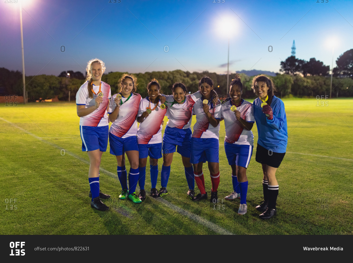 Front view of diverse female soccer team posing with medal at sports field
